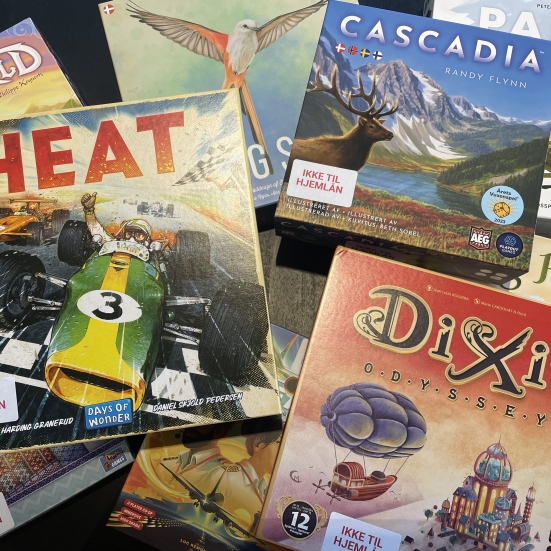 BIllede af forskellige brætspil i en bunke: Heat, Cascadia, Paleo, DiXit, Wingspan og andre man ikke kan læse titlerne på. 