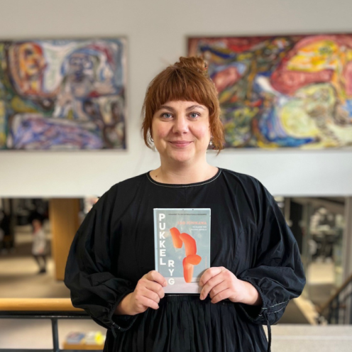 Formidler Emma i biblioteksrummet foran Asger Jorn malerierne med romanen "Pukkelryg" i hænderne